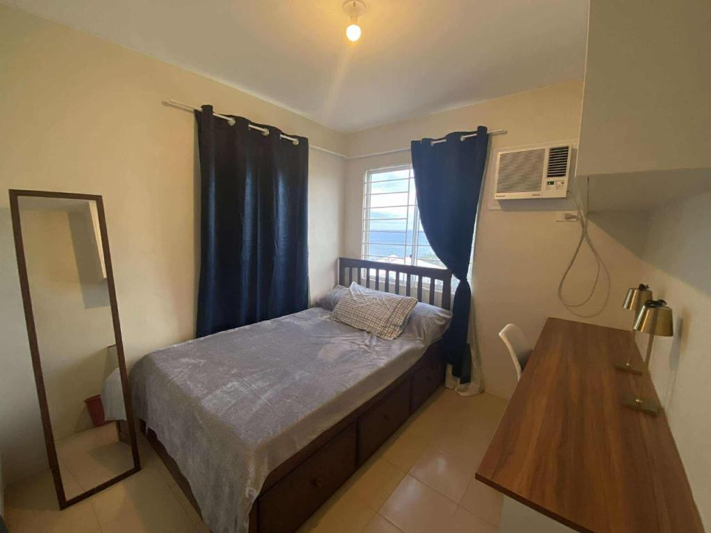 a bedroom with a bed with blue curtains and a table at Kaira's Condo at Marina Spatial 2 BR WIFI Netflix in Laguna
