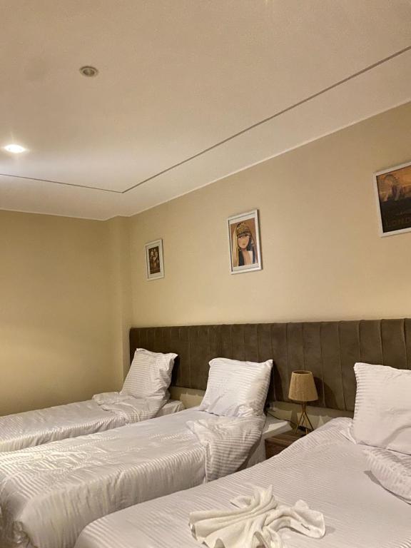 Una habitación de hotel con tres camas con sábanas blancas. en Pyramids Hotel & Free pickup shuttle, en El Cairo