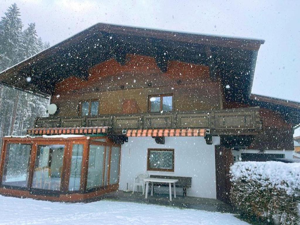 Una casa cubierta de nieve con un banco delante de ella. en Landhaus am Waldrand, en Oberndorf in Tirol