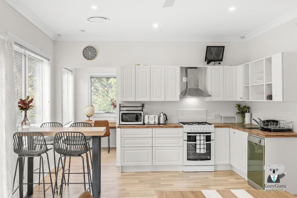 Una cocina con gabinetes blancos y una mesa y sillas. en KozyGuru | Erina | Sunny Coastal Escape + Parking, en Erina East