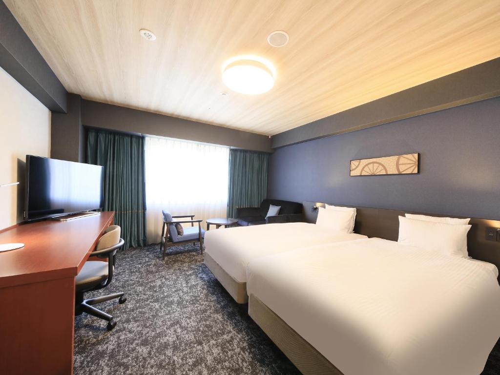 a hotel room with two beds and a desk at Richmond Hotel Yokohama-Bashamichi in Yokohama