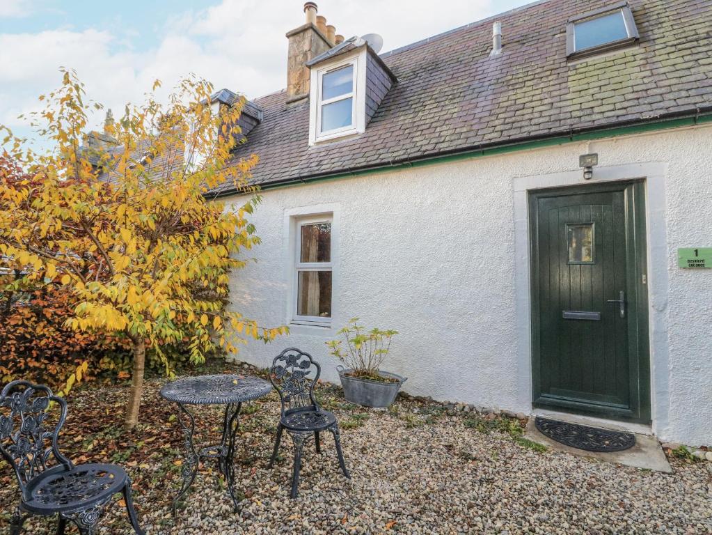 a white house with a green door and chairs at Deskford Cottage in Balblair