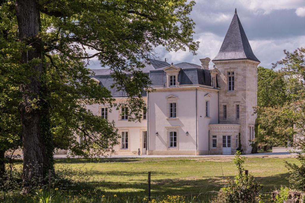 a large white house with a tower on a field at Château Sénéjac in Le Pian-Médoc
