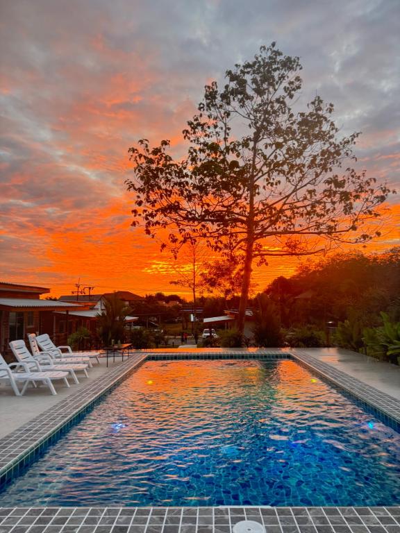 een zwembad met stoelen en een zonsondergang op de achtergrond bij Forest Hill Lanta in Koh Lanta