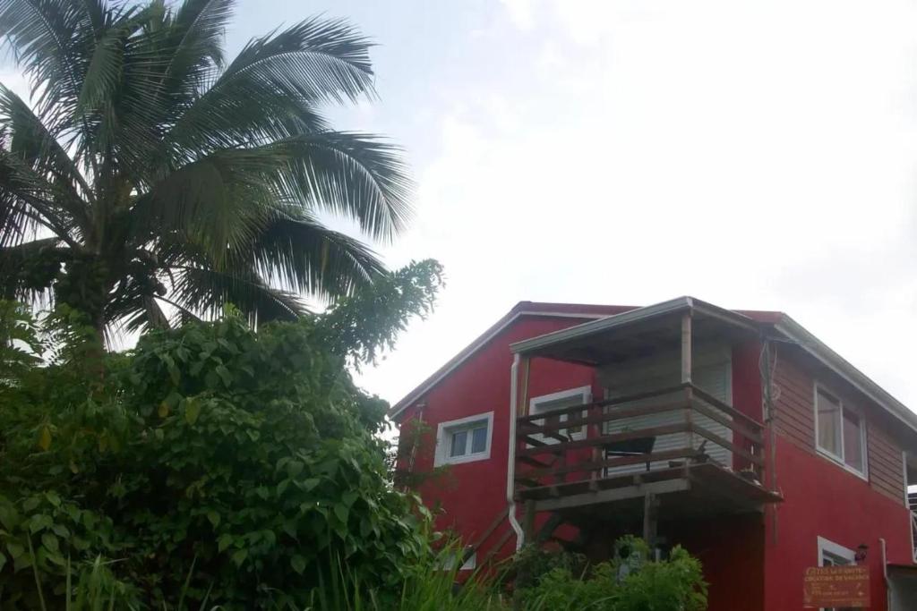 a red building with a palm tree in front of it at Appartement avec Terrasse à Capesterre-Belle-Eau in Petites Mamelles