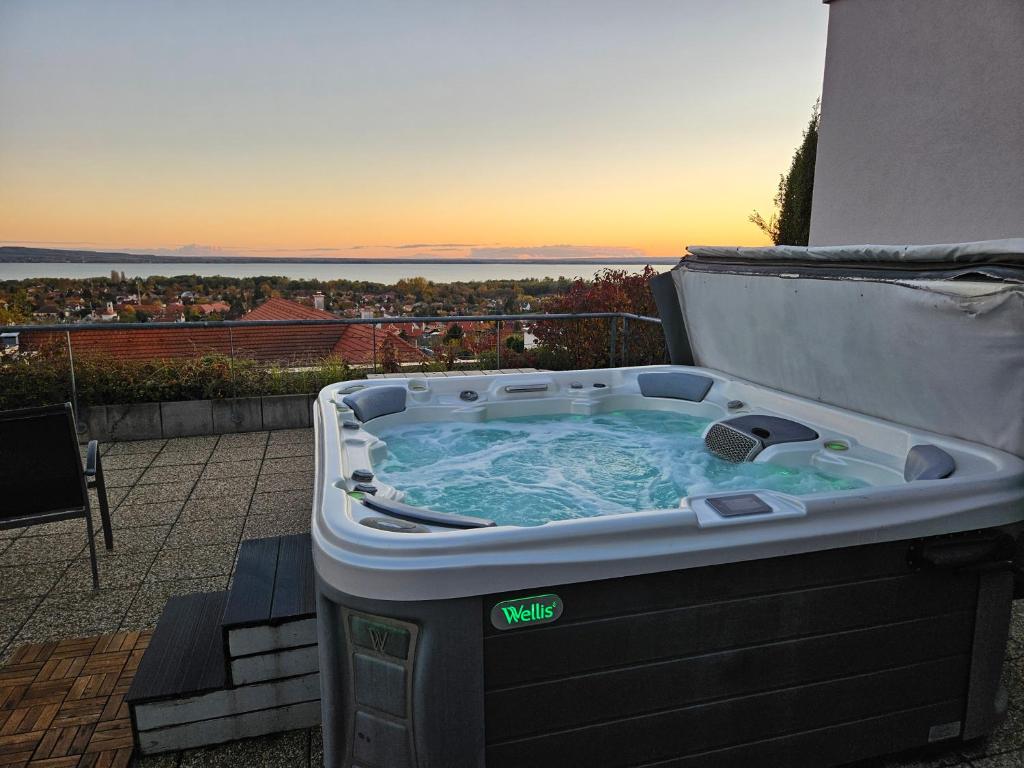 a hot tub on a balcony with the sunset in the background at Zenit Wellness Hotel Balaton in Vonyarcvashegy