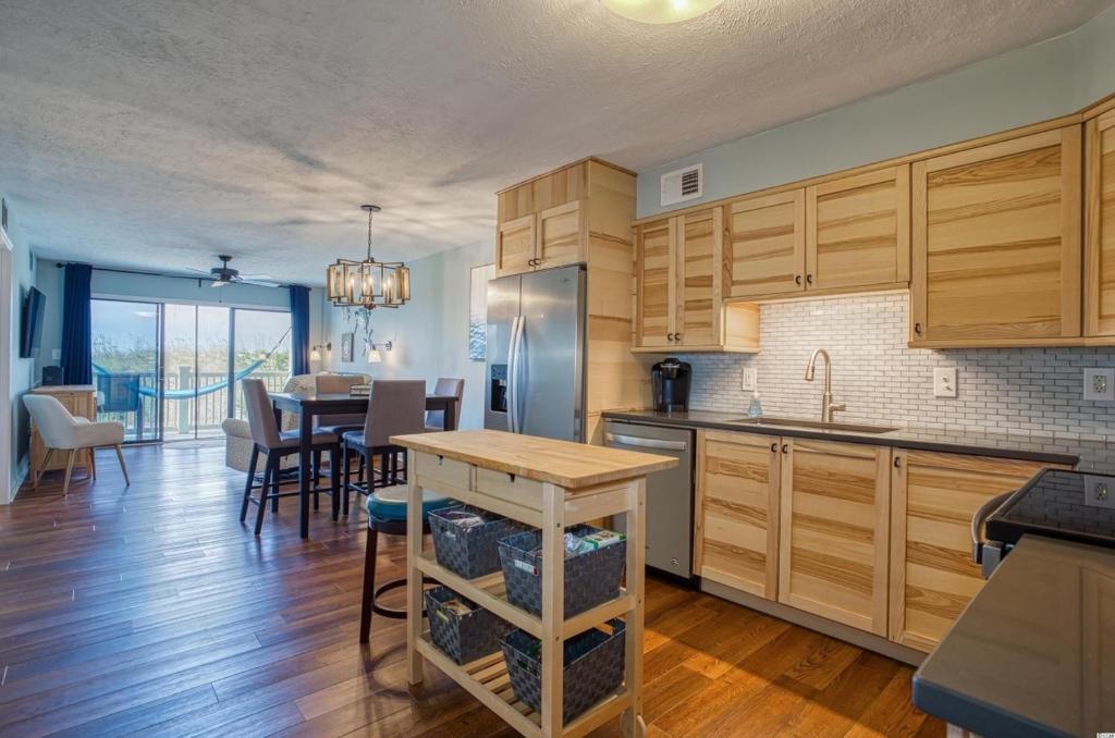 Una cocina con gabinetes de madera y un comedor. en BEAUTIFUL BEACHFRONT-Oceanfront First Floor 2BR 2BA Condo in Cherry Grove, North Myrtle Beach! RENOVATED with a Fully Equipped Kitchen, 3 Separate Beds, Pool, Private Patio & Steps to the Sand!, en Myrtle Beach