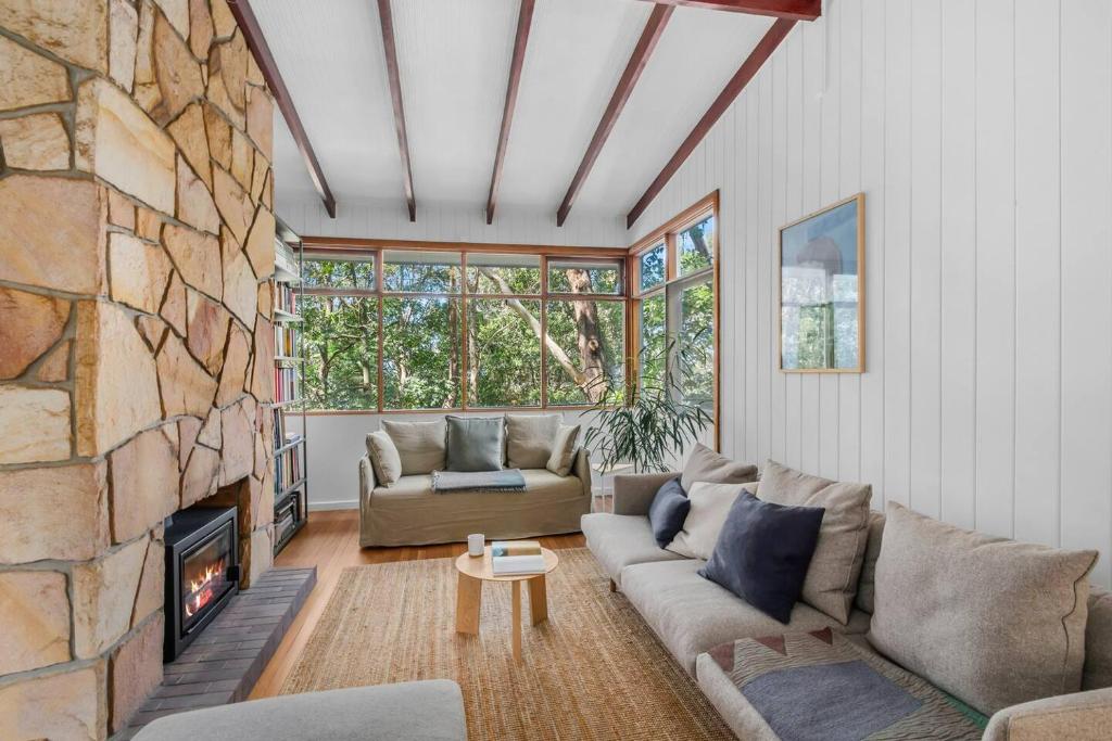 a living room with a couch and a stone fireplace at Forest Trails Escape - Bushland Serenity near Beach in Austinmer