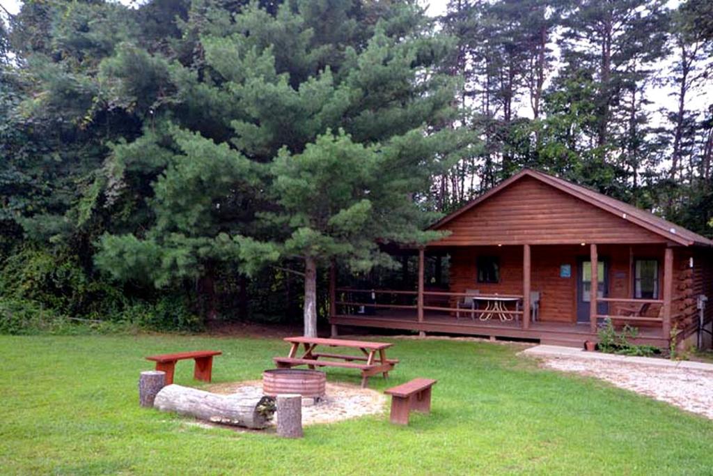 a log cabin with picnic tables in the grass at Charming Log Cabin with a Fire Pit in the Woods near Lake Logan in Ohio in Cedar Grove