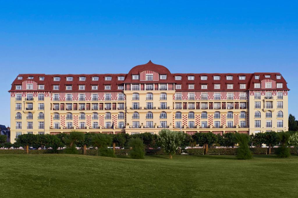 a large building with a green field in front of it at Hôtel Barrière Le Royal Deauville in Deauville