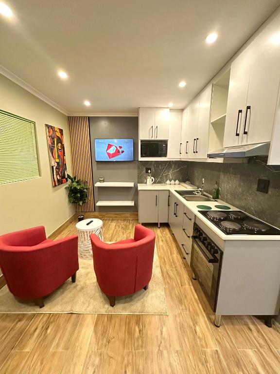 a kitchen with white cabinets and red chairs and a tv at 29 Windsor Flatlet 2 in Silver Sands