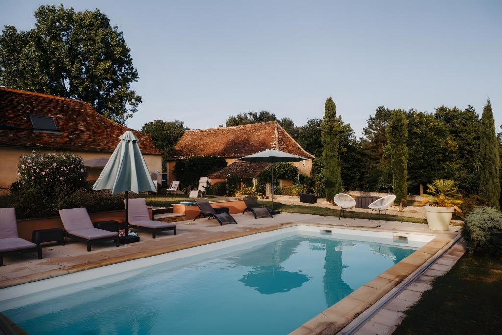 a swimming pool with chairs and an umbrella next to a house at Lodge La Forêt in Saint-Sauveur