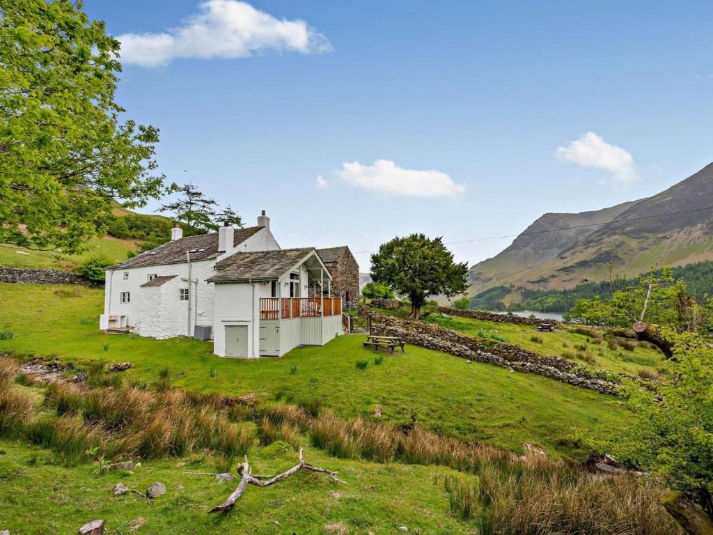 a white house on a green hill with mountains in the background at 4 Bed in Buttermere SZ090 in Buttermere