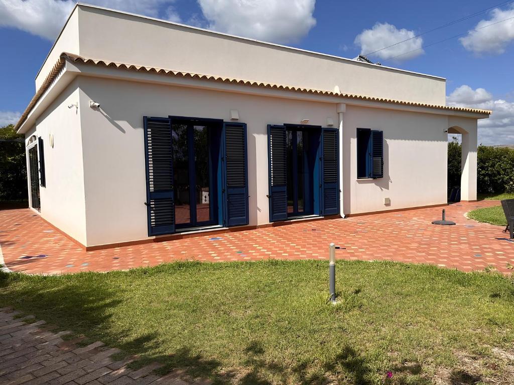 a white house with blue shutters on a brick yard at Villa Gioconda a 200metri spiaggia Noto Calabernardo in Calabernardo