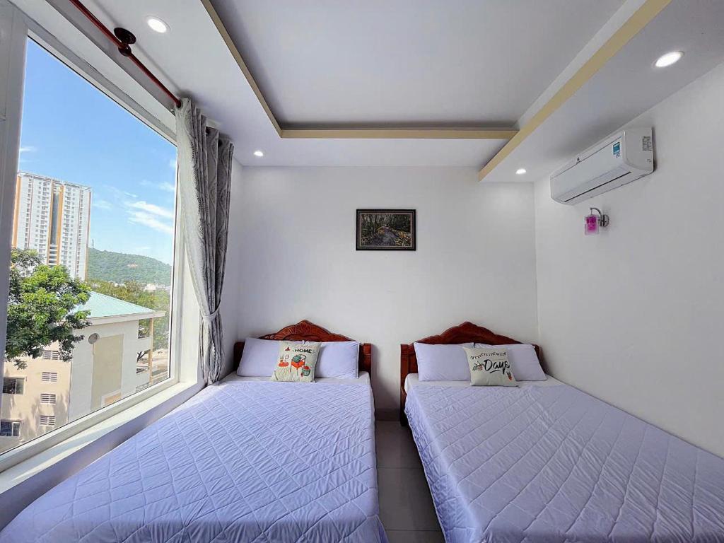 two beds in a room with a large window at New Star Hotel Vũng Tàu in Vung Tau