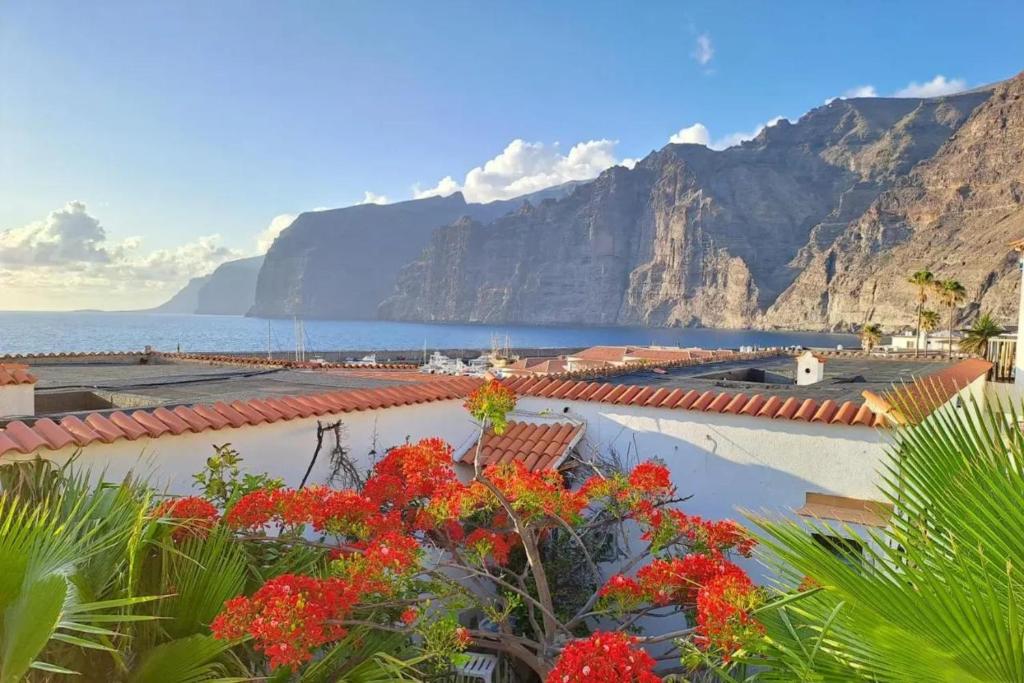 a view of the ocean and mountains with red flowers at Cozy apartment with sea view - 70 m² in Acantilado de los Gigantes