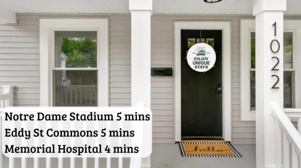 a white house with a black door and a sign on it at Sweet Retreat 3 Mins to Notre Dame Eddy St Commons and Memorial Hospital in South Bend