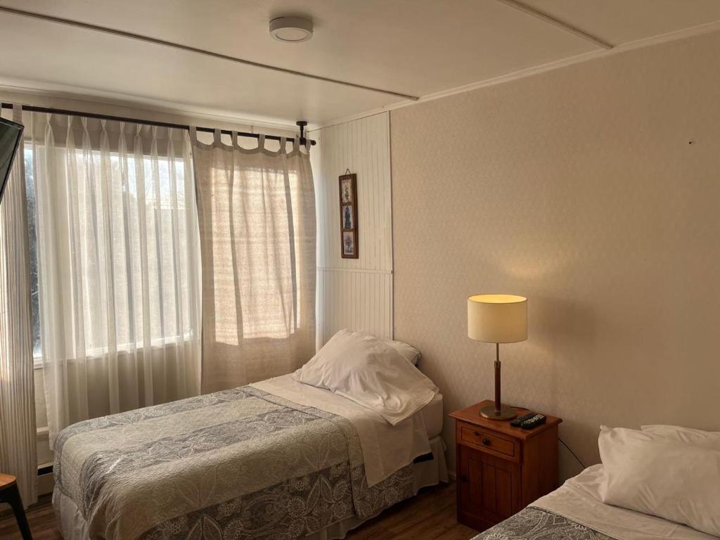Un dormitorio con dos camas y una lámpara y una ventana. en Gran Via Hostel, en Punta Arenas