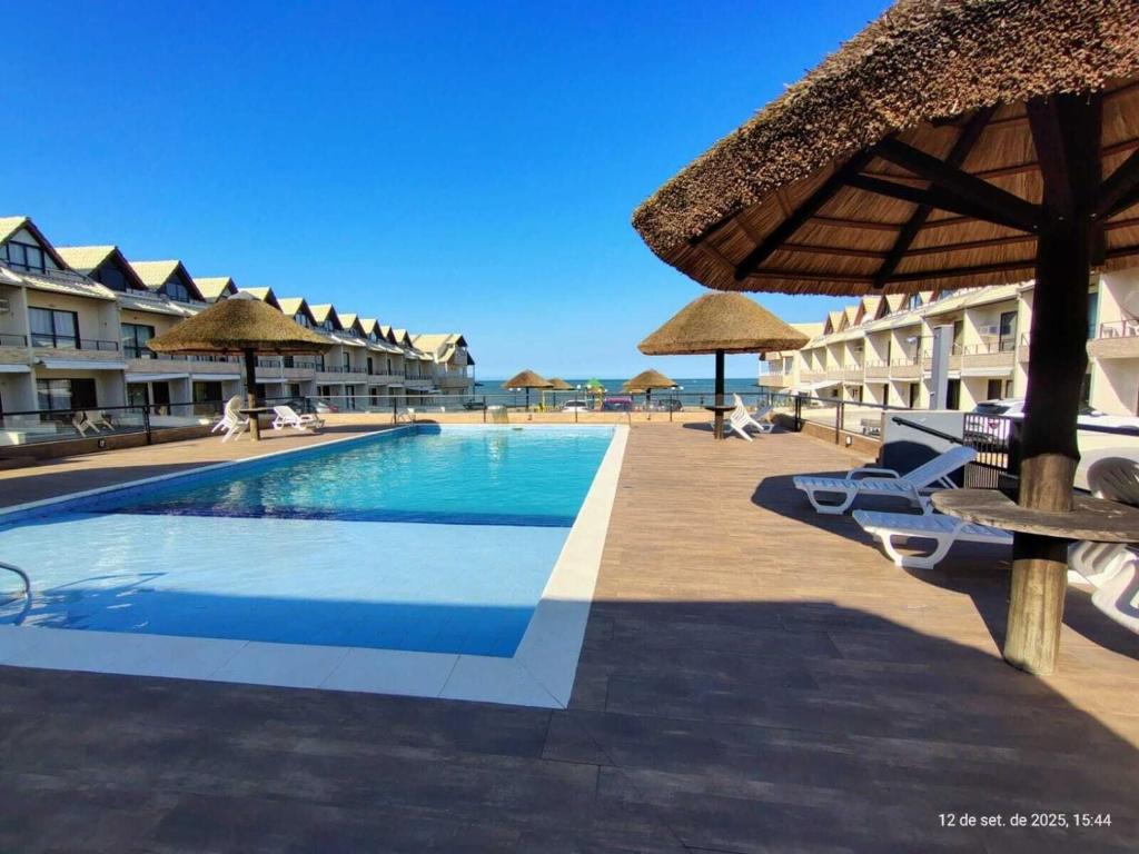 a swimming pool with chairs and umbrellas at a resort at Casas em condomínio a Beira-Mar com piscina, Itajubá - MCSs in Itajubá