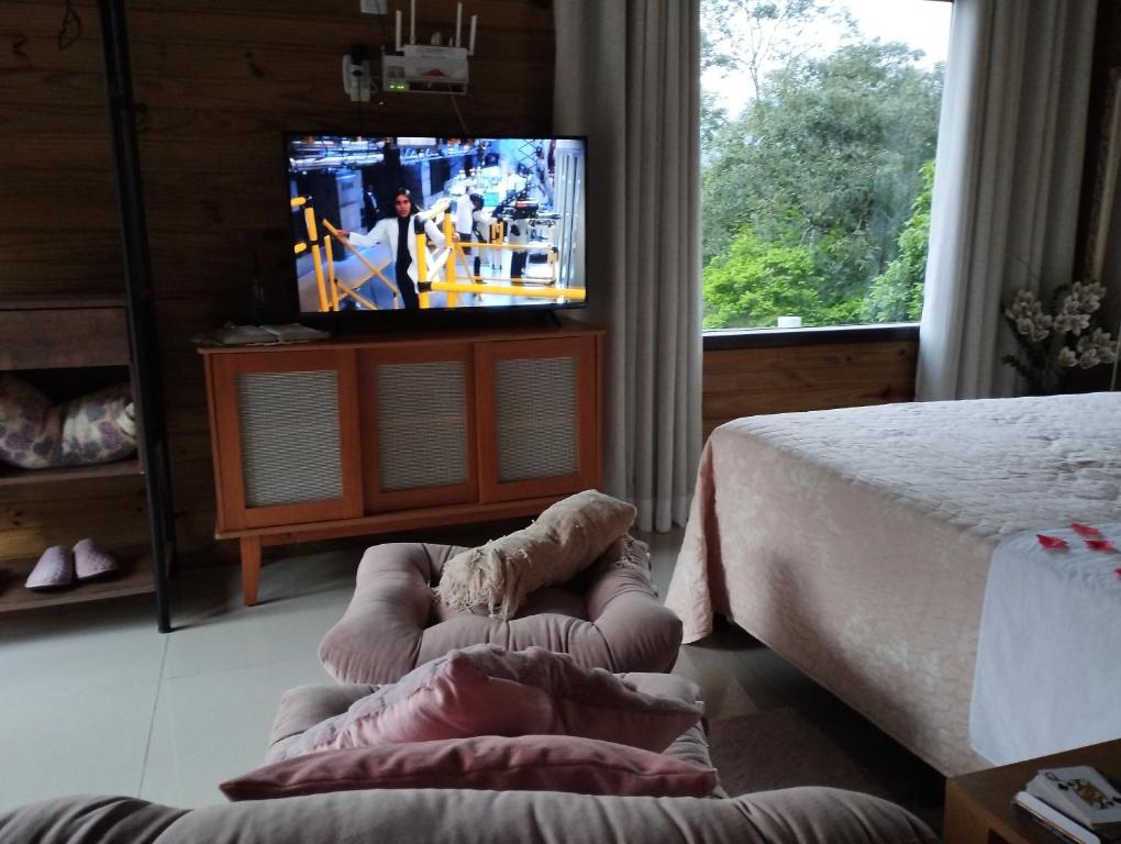 ein Schlafzimmer mit einem Bett, einem Fernseher und einem Stuhl in der Unterkunft Morro do Eurico - Descanso e privacidade in Praia Grande