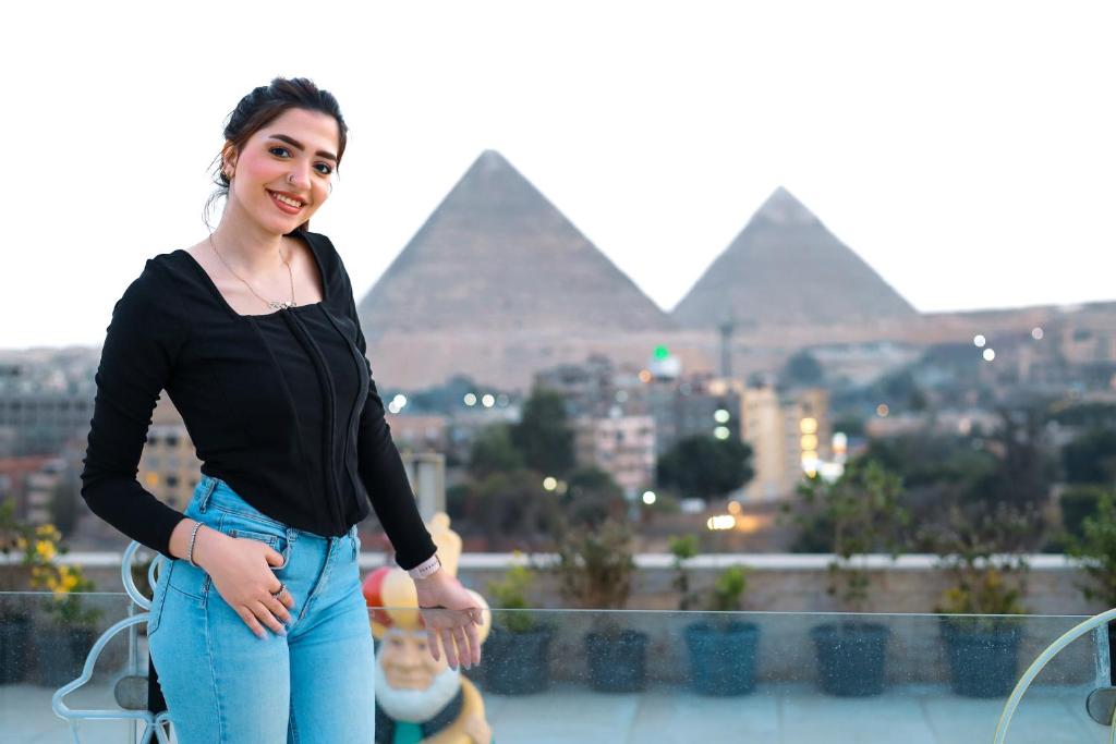 een vrouw op een balkon met piramides op de achtergrond bij The Muse Luxury View Hotel in Caïro