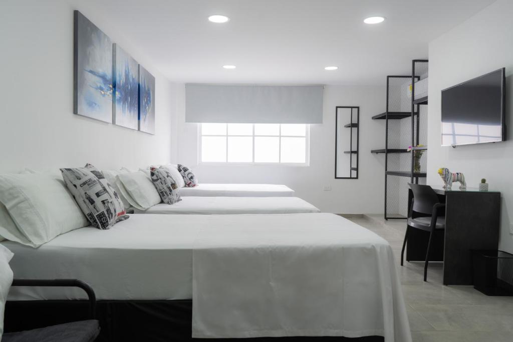 ELEGANTE, CÓMODO Y MODERNO APARTAMENTO - SUR DE CALI في كالي: غرفة بيضاء مع أربعة أسرة وتلفزيون