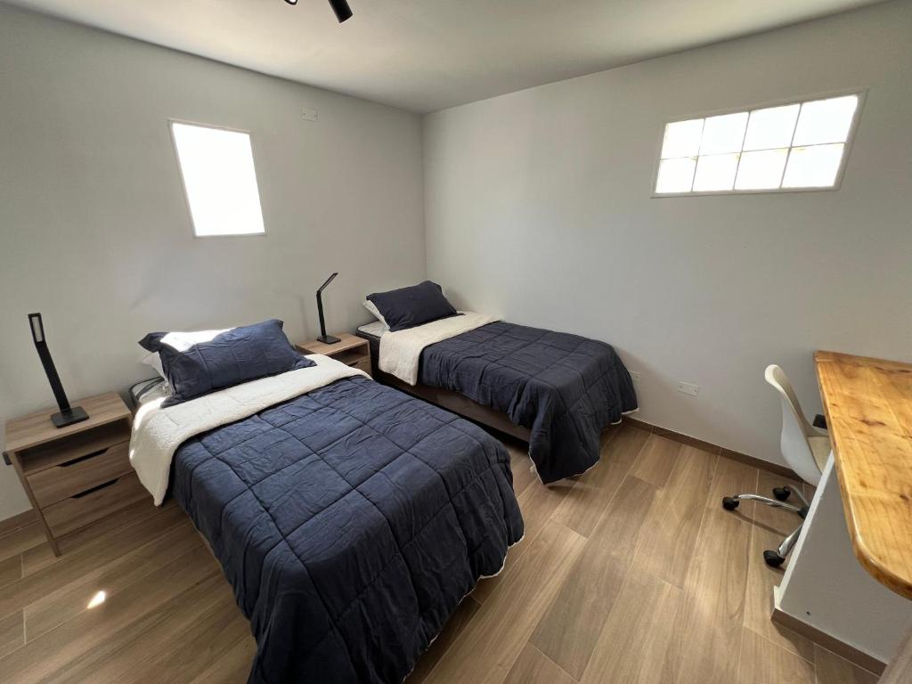 a bedroom with two beds and a desk and two windows at AH Residencial in Antofagasta