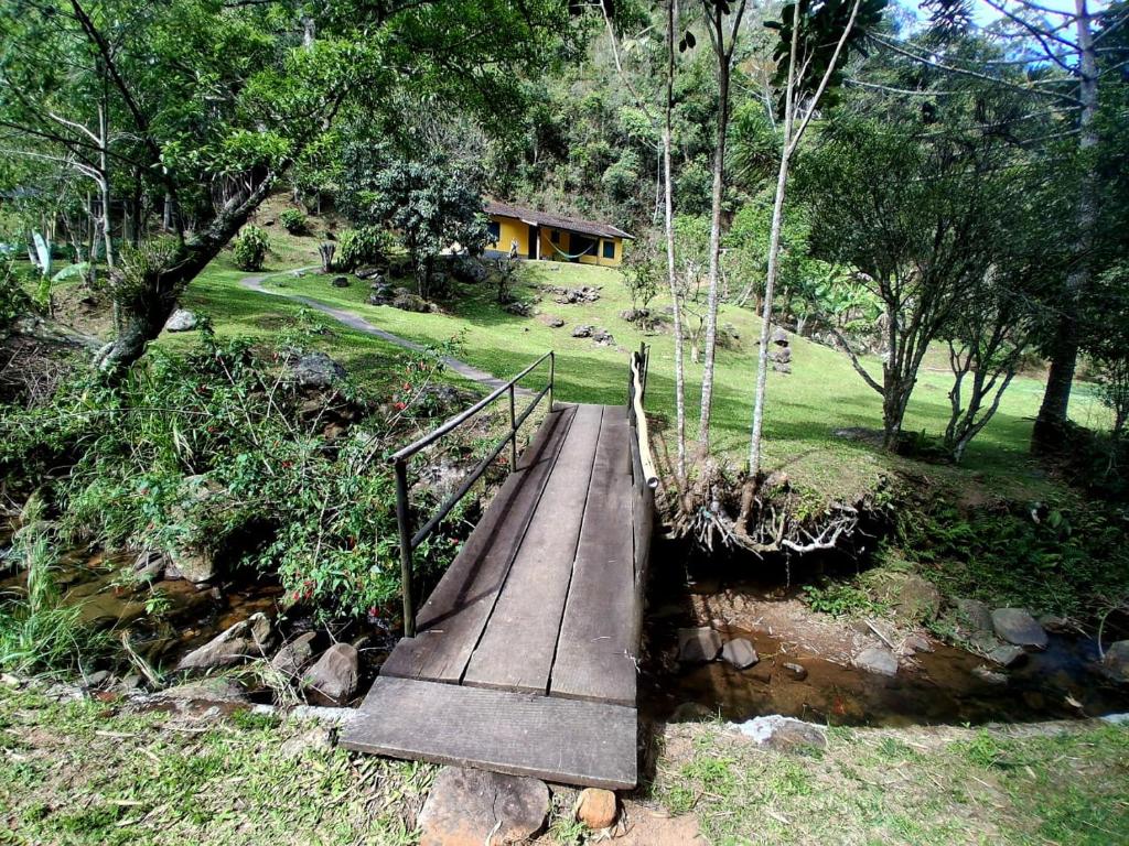 un puente de madera sobre un río con una casa en el fondo en Sítio Toca da Onça- Lumiar, en Nova Friburgo