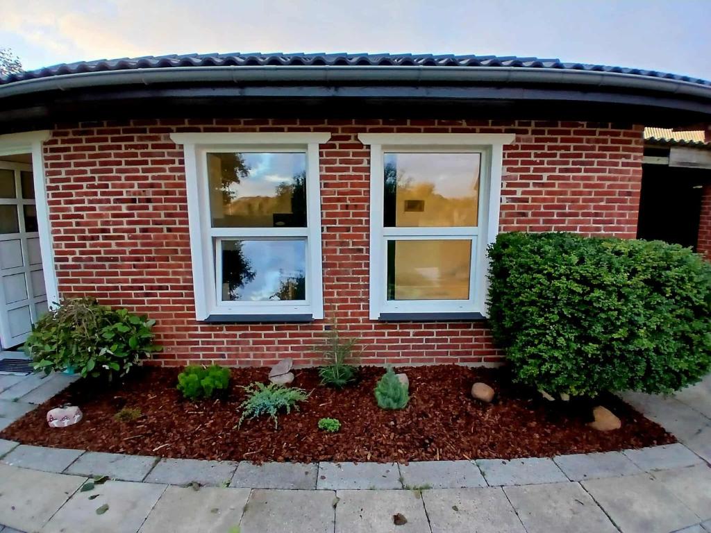 a red brick house with two windows and plants at Cozy Cottage Near the Skjern River in Tarm