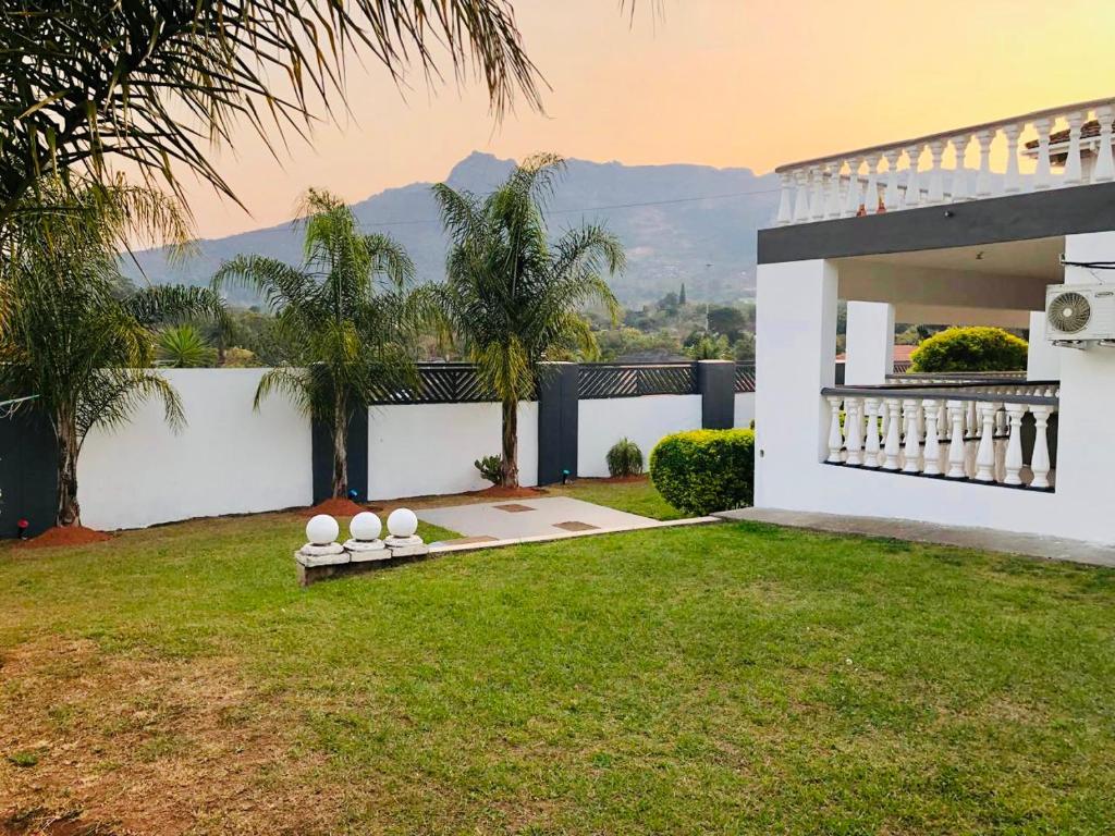una casa blanca con un patio con césped y palmeras en Grand Tranquil Views, en Lobamba