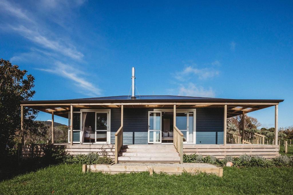 une maison bleue avec une terrasse couverte sur une pelouse dans l'établissement Weld Cottage - Sustainable lifestyle property, à New Plymouth