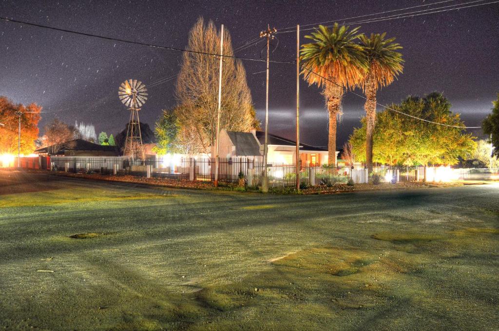 an empty street at night with a windmill and palm trees at Rose Acres Guest House in Parys