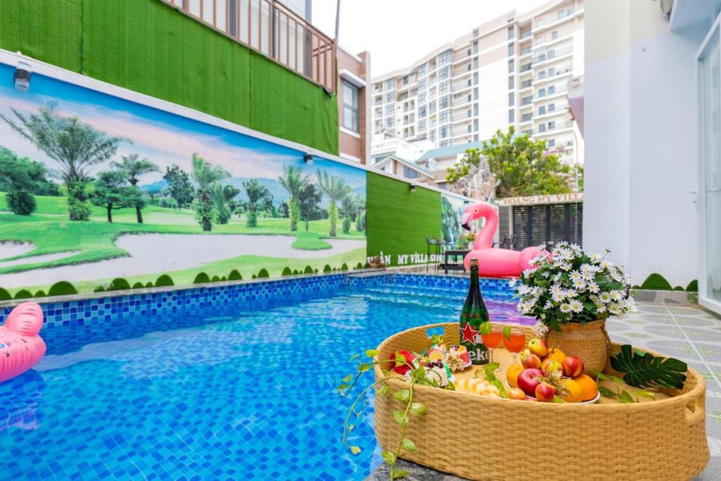 a pool with a table with fruit and a pink flamingo at Hoàng My Villa - 100m tới bãi tắm Long Cung in Vung Tau