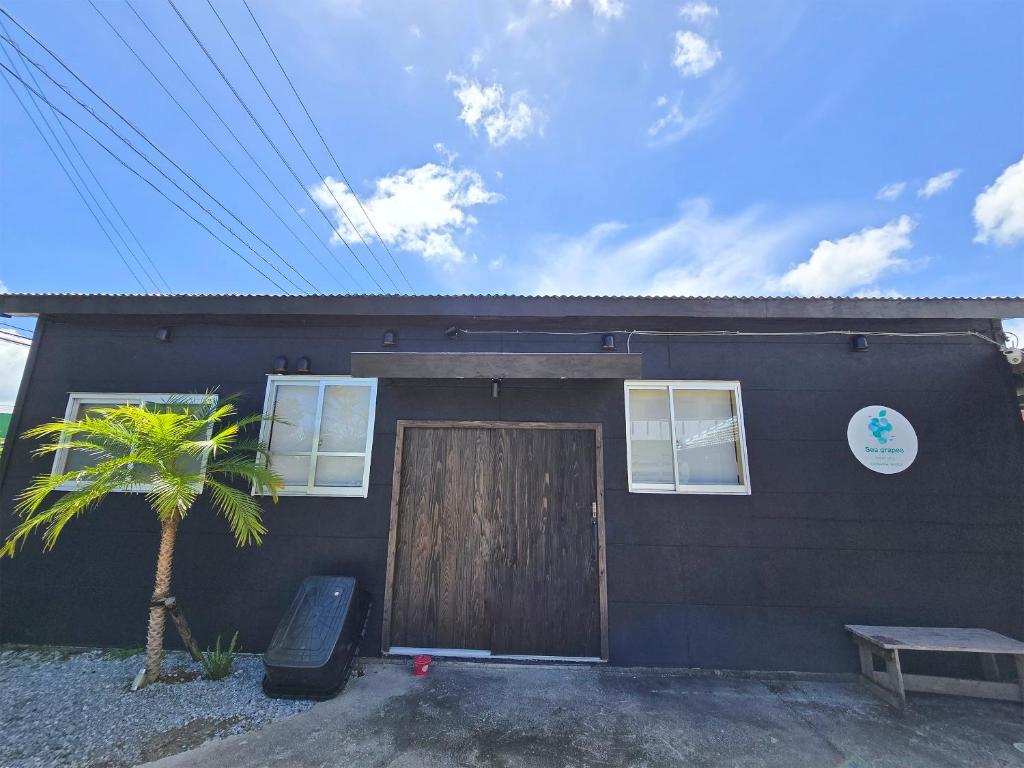 una casa nera con una porta di legno e una palma di Petit villa Sea grapes a Nago