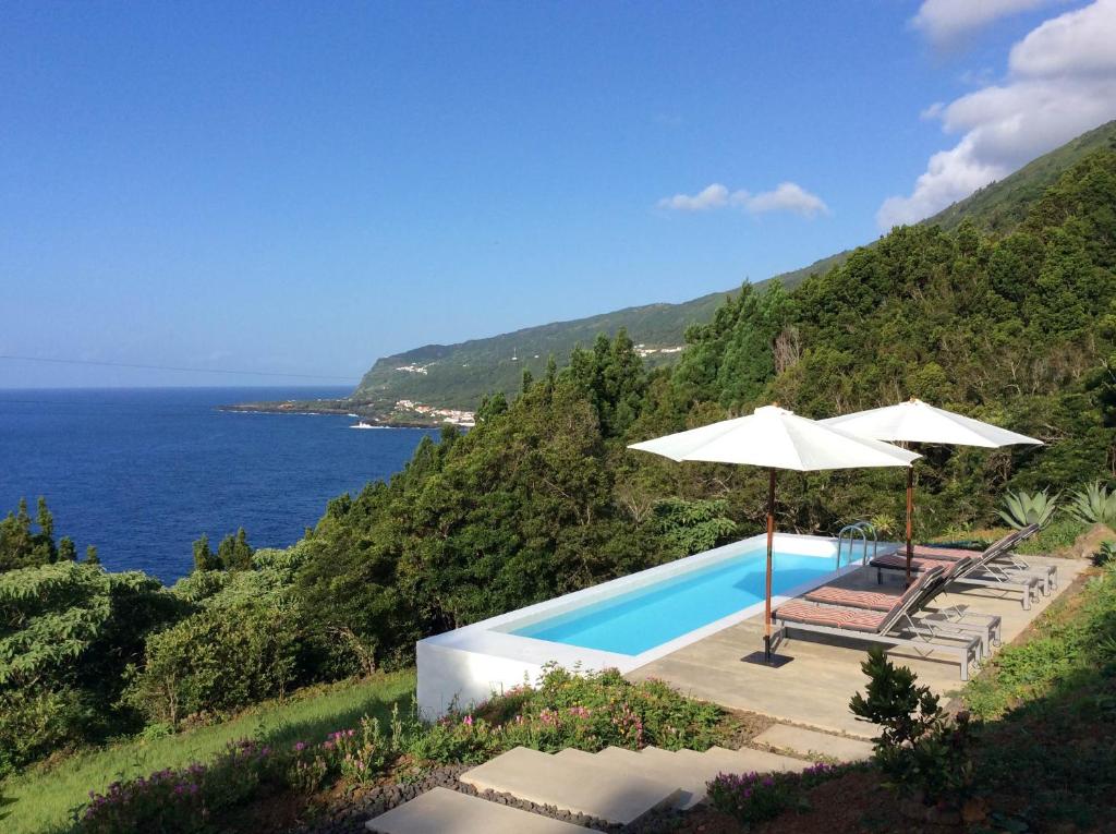 una piscina con sombrilla y sillas y el océano en Casas de Incensos - TER -TA en Pontas Negras