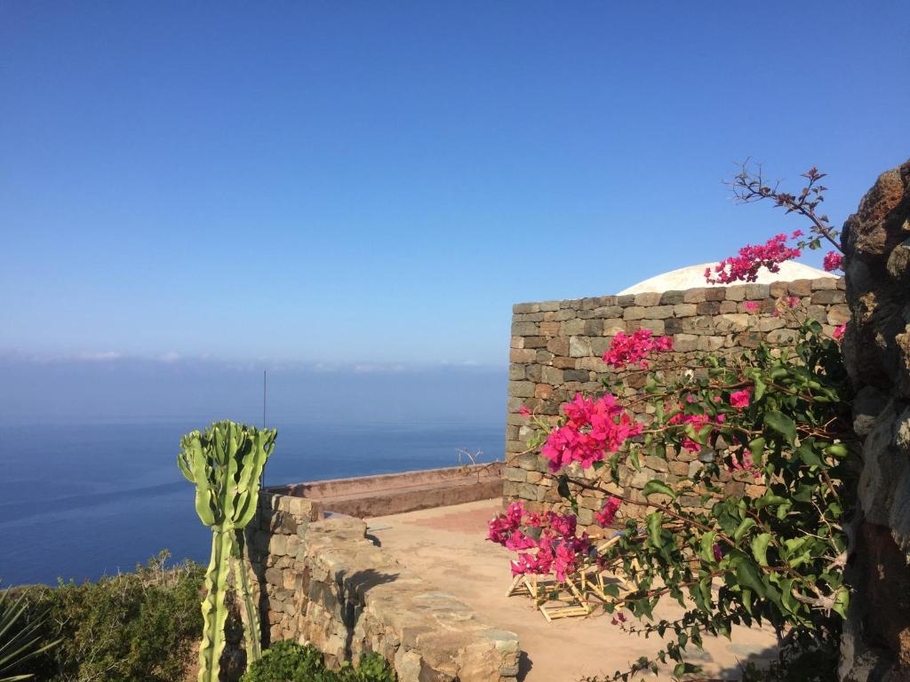 a stone wall with pink flowers and the ocean at Dammuso Il Sogno in Scauri