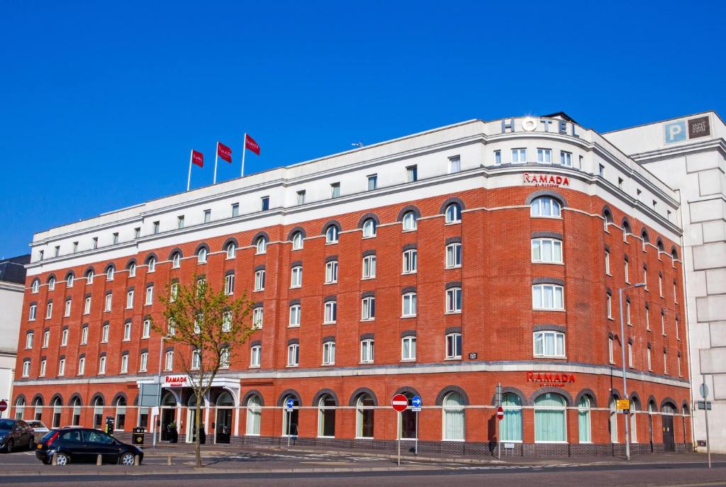 a large red brick building with two flags on top at Ramada by Wyndham Belfast in Belfast