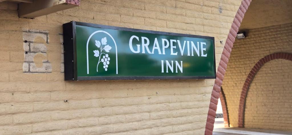 een groen bord op een bakstenen muur met een druivenranklijn bij Grapevine Inn in Lodi