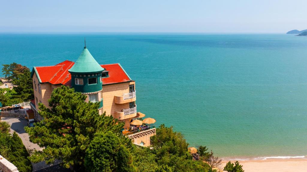 een gebouw met een rood dak naast de oceaan bij Qingdao Momer Cliff Ocean View Villas in Qingdao