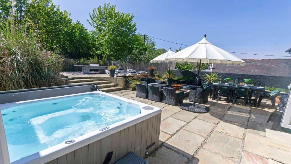 un jacuzzi dans un patio avec une table et un parasol dans l'établissement Shippenrill Croyde - Sleeps 14 - Hot Tub option - Stylish Home with fire pit, table tennis & dog friendly, à Croyde