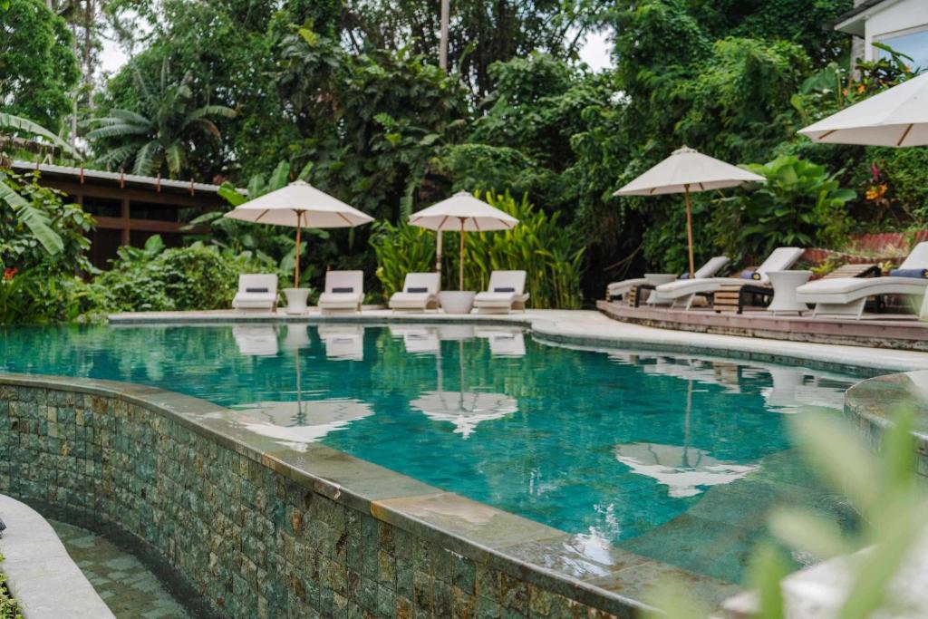 a swimming pool with chairs and umbrellas at Hot Stone Club Ubud in Ubud