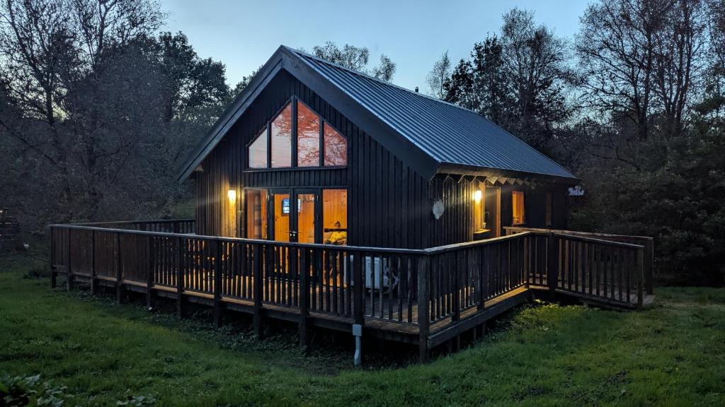 a small cabin with a large deck in a field at Bracken Lodge in Dalavich
