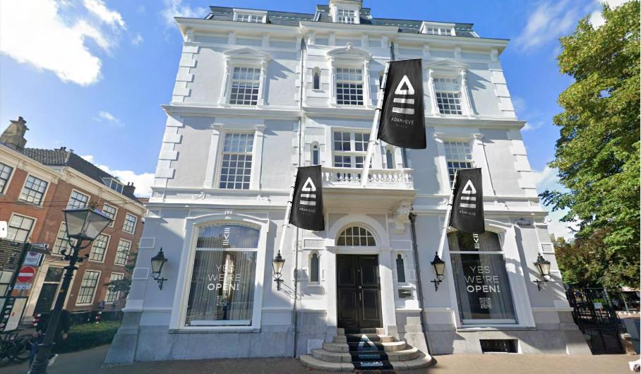 een wit gebouw met zwarte vlaggen ervoor bij ADAM & EVE Paleisstraat in Den Haag