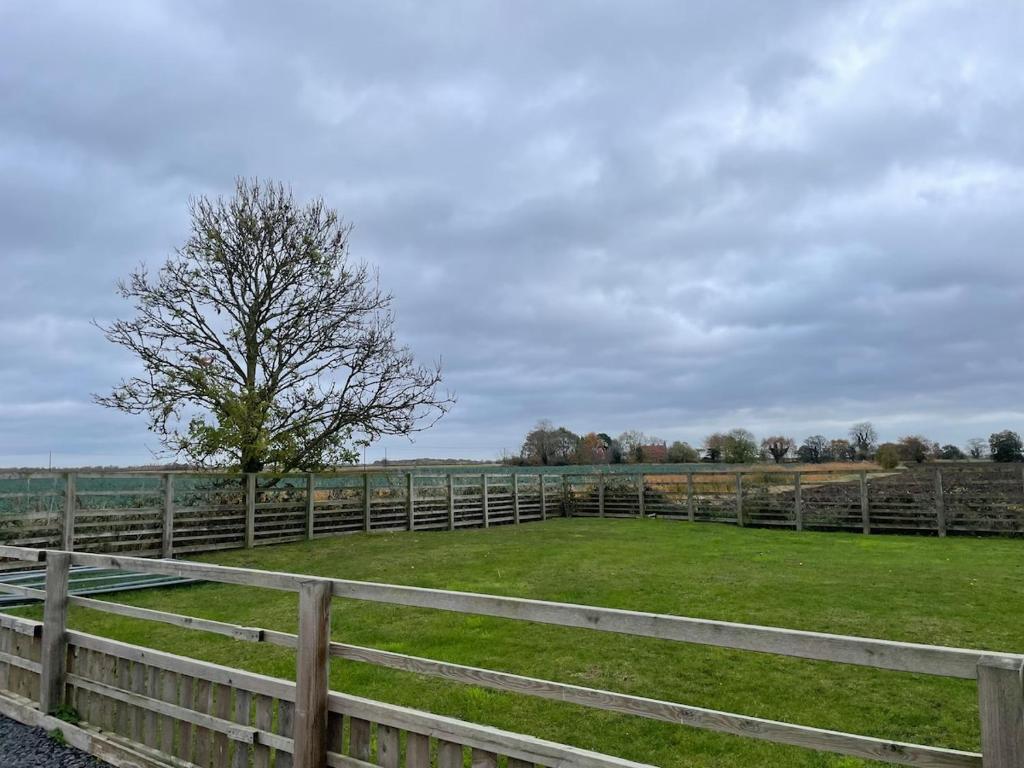 a fence with a tree in the middle of a field at Three bedroom cabin with rural views and hot tub in Algarkirk
