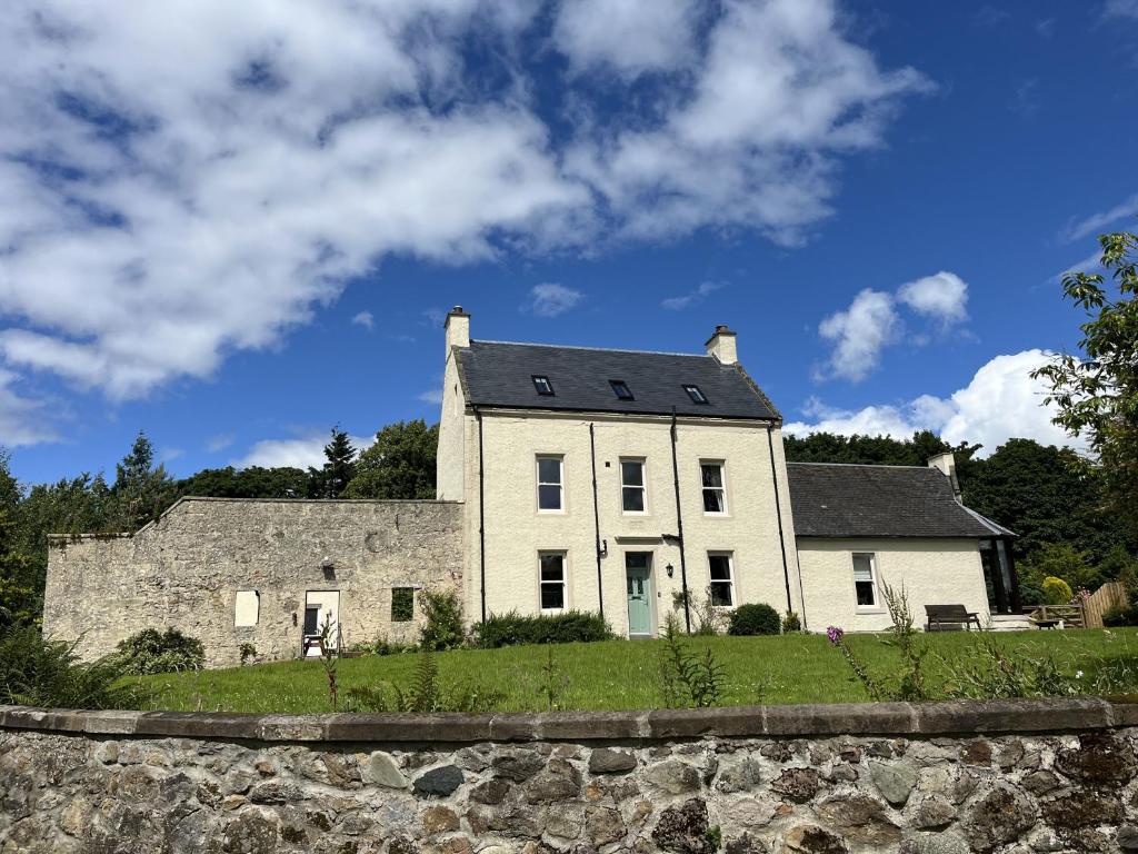 una casa blanca en una colina con un muro de piedra en The Farmhouse at Solsgirth Home Farm, en Dollar