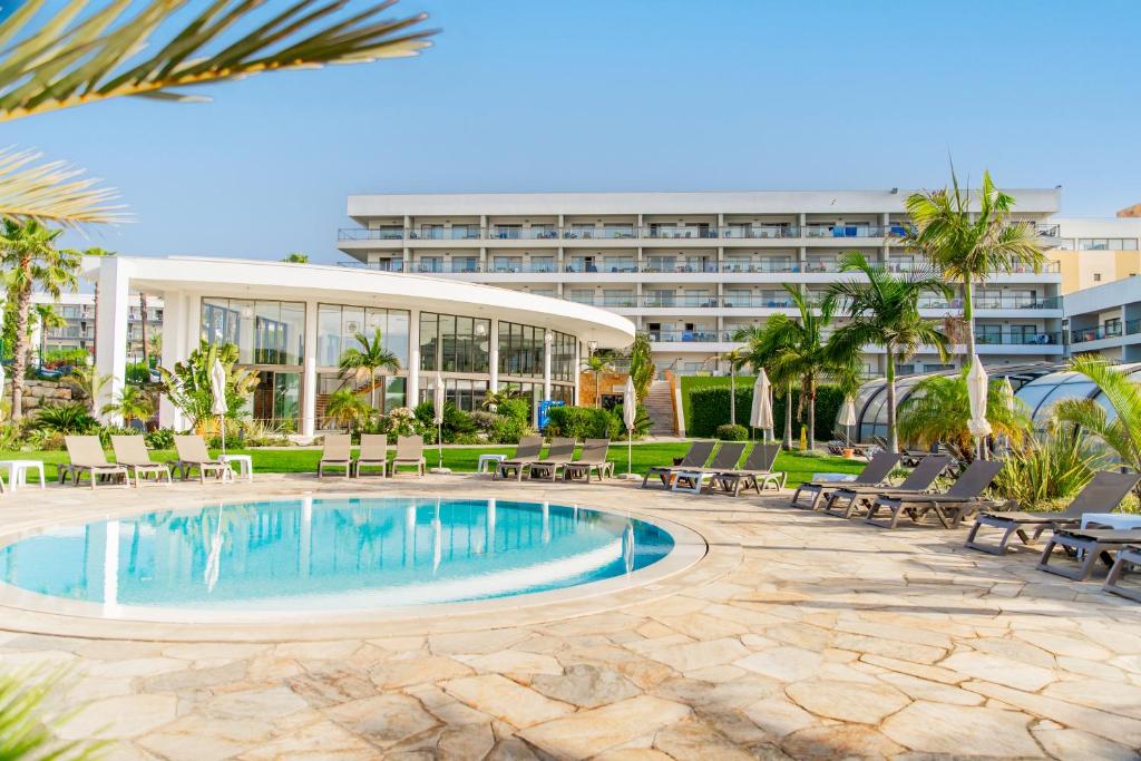 a resort pool with chairs and a hotel in the background at Alfagar Prestige in Albufeira