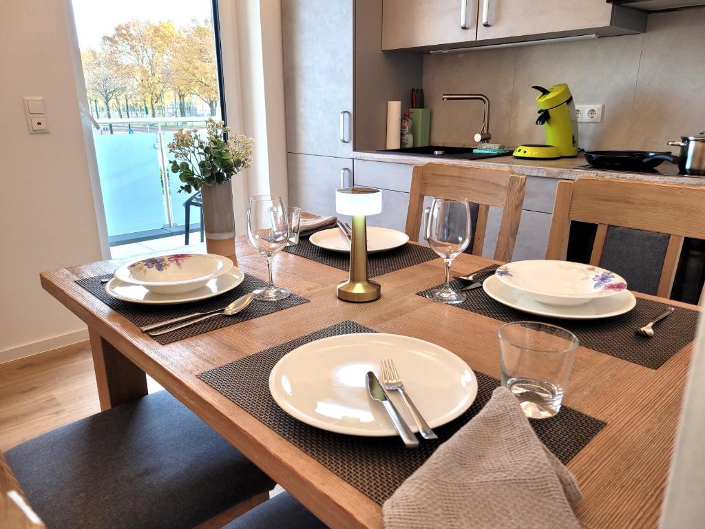 Una mesa de madera con platos y copas de vino encima. en KomfortPlus modernes Premium Apartment - Top Lage - Balkon - Parkplatz, en Bad Zwischenahn