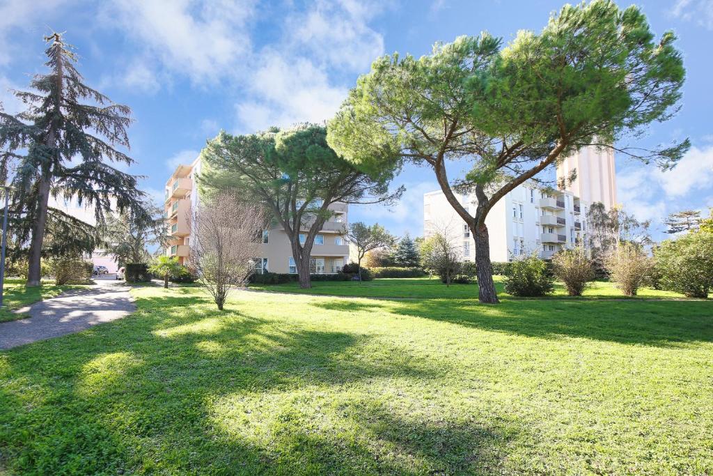 a green park with trees and buildings in the background at Riverside Toulouse (Savory) in Blagnac