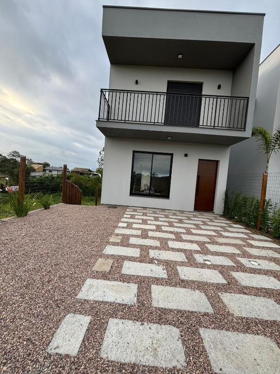 a white house with a balcony and a stone driveway at Tua Casa no Rosa in Imbituba