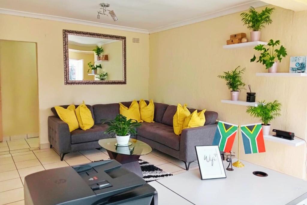 sala de estar con sofá gris y almohadas amarillas en Budget Stays at Olivia Pines Guesthouse, en Krugersdorp